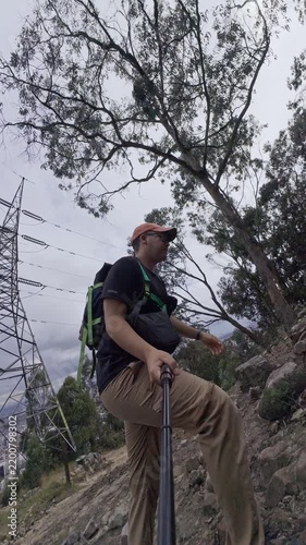 Hiker Filming Himself On Rocky Trail Near Power Lines Under Eucalyptus Trees With Overcast Sky.