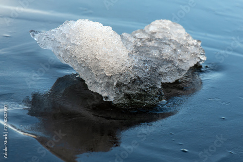 Foto Creative macro photograph of a melting ice fragment shaped exactly like a small creature or fox, sitting on dark blue frozen water surface