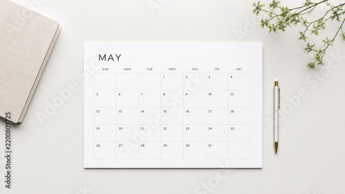 Minimal flat lay of a May calendar page on a white desk with pen, notebook and a small sprig of greenery for planning and organization