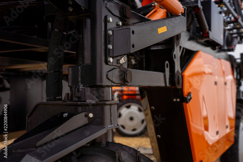 Close-up of heavy duty suspension and black steel chassis of modern agricultural machinery, showing hydraulic hoses, bolts, and orange body panels.