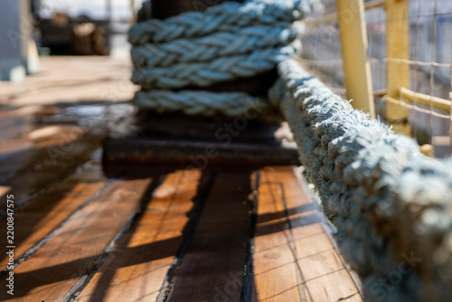 Obraz na płótnie Mooring rope secured around steel bollard on wooden ship deck, representing nautical vessel equipment, maritime transportation, and harbour boat docking