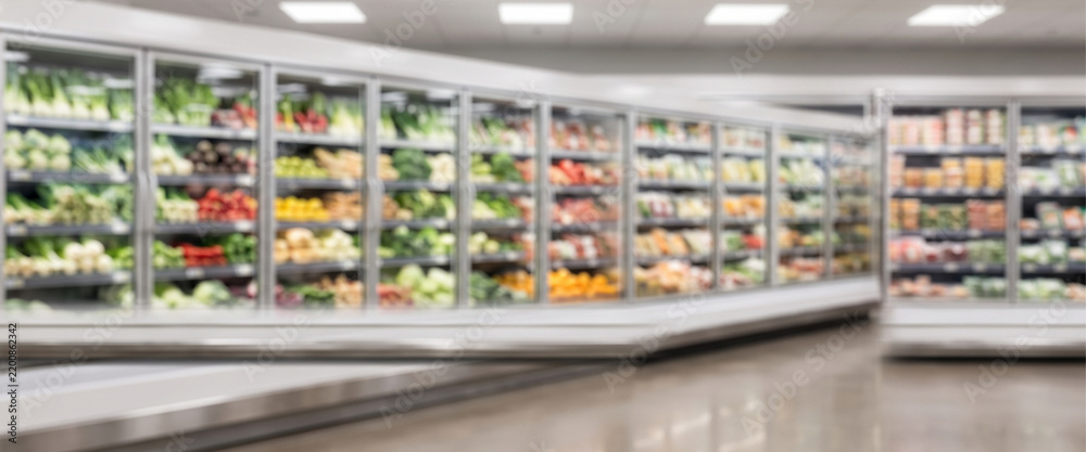 Fototapeta premium Modern supermarket refrigerated produce wall with fresh vegetables, glass displays and bright retail lighting, presented in a uniform full-frame Gaussian blur for commercial grocery backgrounds.