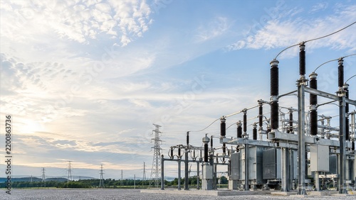 High voltage electrical substation infrastructure with power lines and transformer equipment under a dramatic blue sky at sunset