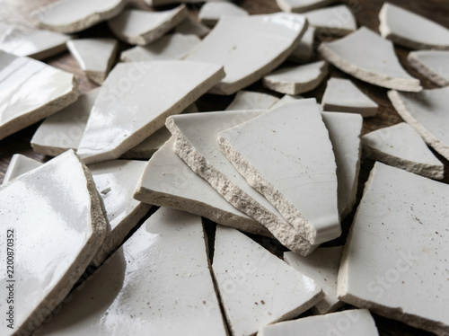 Shattered white ceramic plate pieces. Broken porcelain shards on wooden surface