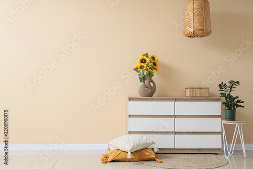 Vases with artificial sunflowers on chest of drawers near beige wall in room ...