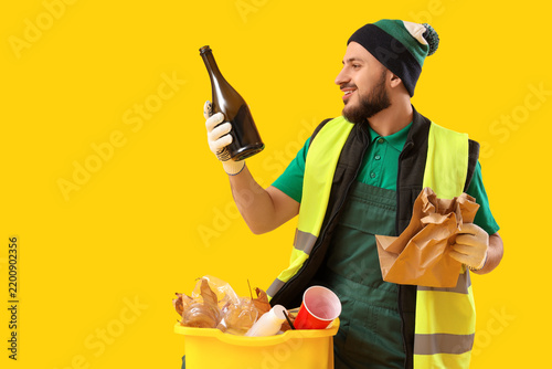 Fotografie Male scavenger with garbage and bin on yellow background