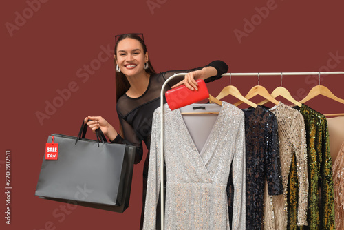Happy young woman with shopping bags, wallet and clothes rack on dark red bac...