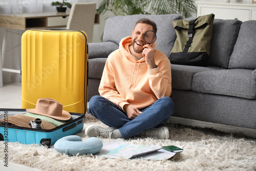 Happy young male tourist with suitcases, map and magnifying glass at home. It...
