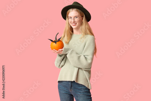 Beautiful young happy woman with Halloween pumpkin and paper bat on pink back...