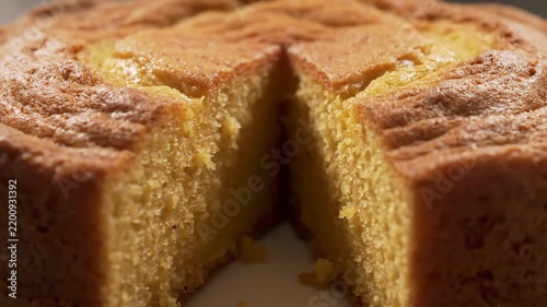 Close-up macro shot of a freshly baked golden sponge cake with a slice removed, highlighting the delicious texture, warm golden color, and detailed crumb.