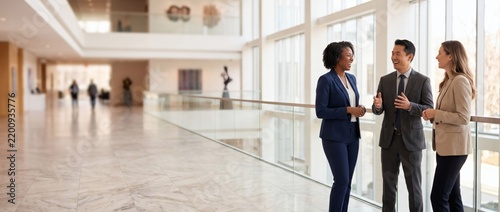 Three business colleagues in suits talking in spacious modern atrium. Corporate executives having professional discussion in glass lobby. Group of company directors. Banner, copy space.