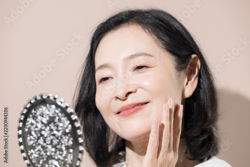 Bild auf Leinwand [Pink Background] A Japanese woman in her 50s checking her cheeks in a mirror; i