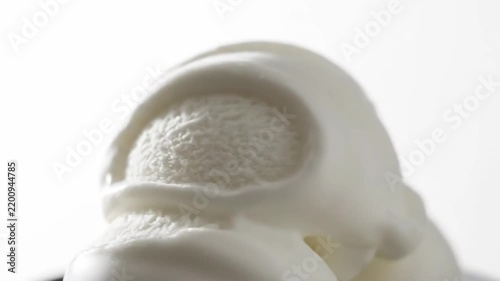 Luxurious Close-Up Shot of Smooth Creamy White Sauce Pouring Over a Scoop of Vanilla Ice Cream Against a Bright High-Key Background.