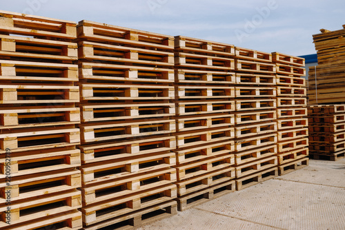 Stacks of weathered wooden pallets arranged in long rows across a paved outdoor storage yard beneath a bright blue sky at an industrial facility