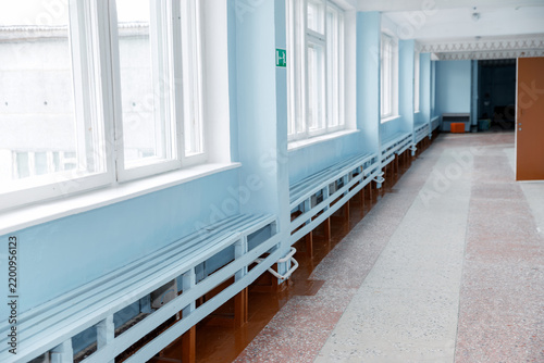 Bright blue school hallway with tall windows, long wall benches, mosaic floors, an open doorway, and school-style decorative trim. concept of education