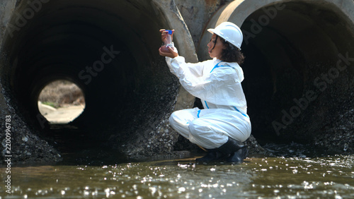 Environmental inspector in protective suit examining wastewater drainage system and industrial water pollution