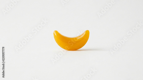 Crescent shaped yellow gummy candy rests horizontally on a neutral transparent backdrop.