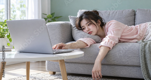 Tired Young Woman Lying on Sofa Reaching for Laptop While Working From Home, Fatigue and Remote Work Burnout Concept