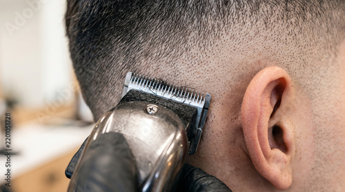 Barber using electric clipper for professional skin fade haircut on client's side head close-up