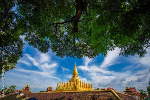 Golden stupa of pha that luang under a blue sky and green tree, vientiane, laos