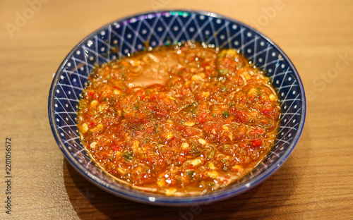 Fotografie Freshly ground spicy chili sambal served in a blue patterned ceramic bowl on a wooden tabletop