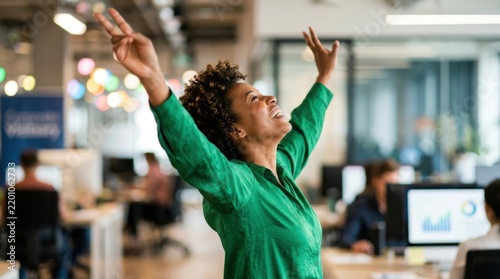 Excited African American businesswoman celebrating success with arms raised high in a modern corporate office workspace environment