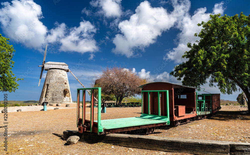 Obraz premium Historic stone windmill and old sugar cane transport train cart at Betty's Hope plantation under a blue sky in Antigua and Barbuda.