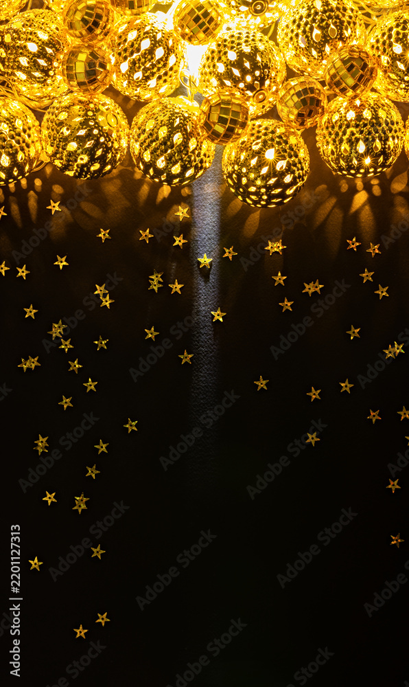 Fototapeta premium Vertical golden Christmas ball lights and scattered stars on black background with copy space for New Year greeting or festive poster