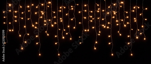Fairy lights hanging garland with warm glow featuring luminous orange and golden bulbs on vertical wires over a dark backdrop for festive Christmas banners and seasonal celebration decor