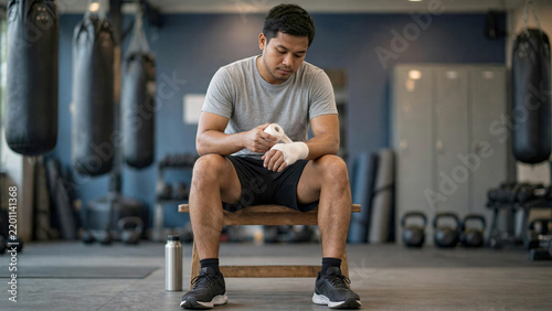 Southeast Asian man wrapping hands thoughtfully while sitting on gym bench