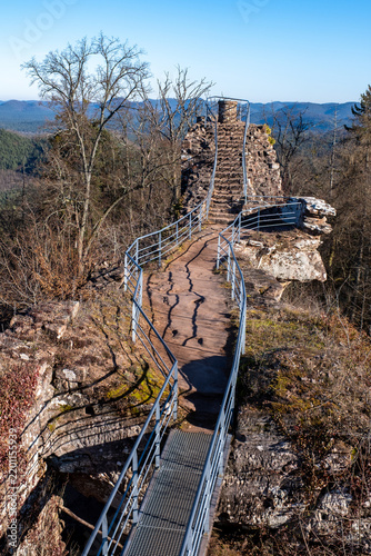 Ruines d'un château médiéval en grès dominant un paysage forestier, avec un sentier aménagé et des montagnes boisées en arrière-plan (château du Falkenstein, France)