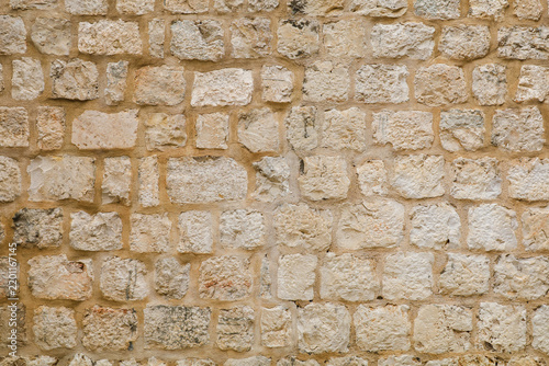 Light beige natural stone wall texture. Ancient rough limestone blocks background. Background of an old fortress wall made of uneven light beige limestone blocks. Rough stone masonry texture