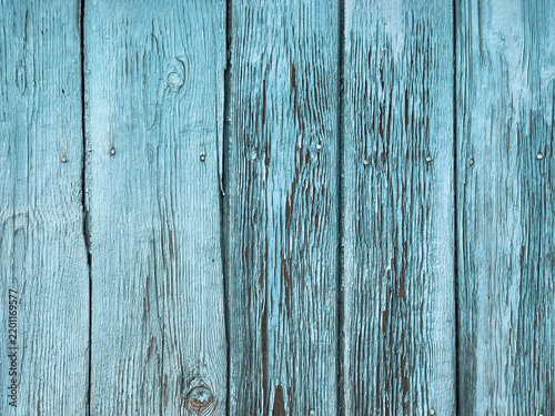 Weathered vertical wooden planks in faded turquoise-blue with pronounced grain, knots, flaking paint, and darkened seams; visible nail heads and natural wood exposure through wear.