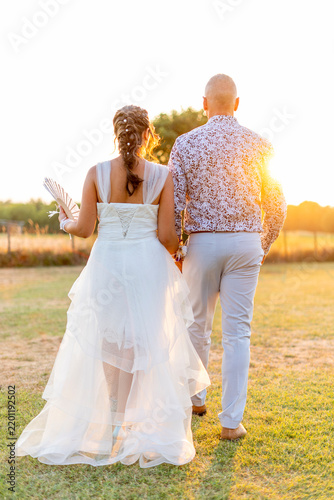 Canvastavla Un couple de jeunes mariés qui marche dans un champ lors d'un couché de soleil c