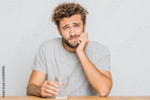 A sad and bored young man with a glass of water at a table. Seasonal blues, seasonal illnesses