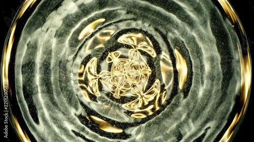 Cymatics wave patterns created by sound frequencies in liquid, forming complex symmetrical golden structures and concentric ripples on a dark background.
