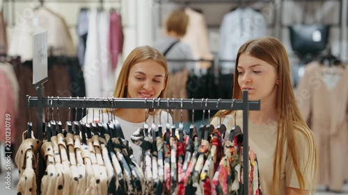 Two women stand closely and examine garments on hangers in fashion store, concept of attention to detail and personal style
