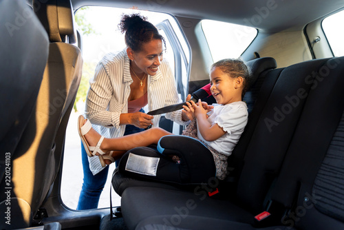 Latino mother securing child in booster seat, ensuring car safety for family travel