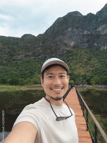 Smiling Asian man takes a selfie on a wooden bridge in southern Thailand's scenic nature.