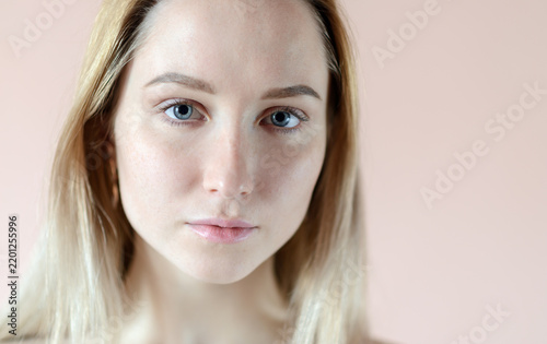 Calm young woman with blue eyes against soft pastel background.