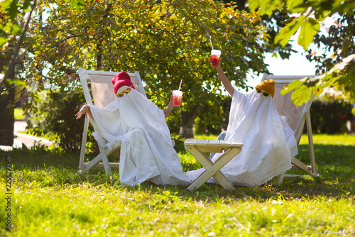 two kids in Halloween ghost costumes Wearing bright hats and black glasses, they drink lemonade in the park. Halloween party