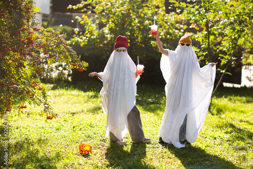 two kids in Halloween ghost costumes Wearing bright hats and black glasses, they drink lemonade in the park. Halloween party