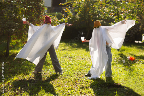 two kids in Halloween ghost costumes Wearing bright hats and black glasses, they drink lemonade in the park. Halloween party