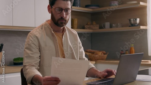 Serious Caucasian business man paying bills online laptop in kitchen busy businessman checking finances reviewing mortgage payments budget paperwork homeowner freelancer using banking website computer
