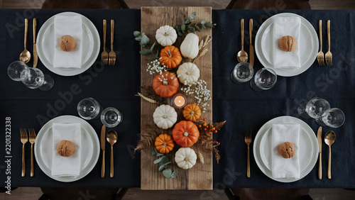 Top view of a rustic thanksgiving table setting with pumpkins, eucalyptus, and gold cutlery on a dark blue tablecloth