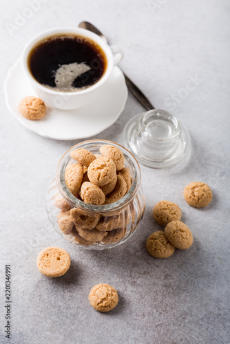 Amaretti cookies in glass pot with white cup of coffee on light gray background with copy space. High angle view