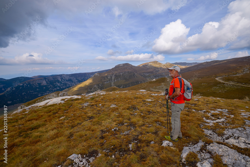 Obraz premium a 75-year-old man hiking in the mountains with poles, a backpack, and mountain gear on a beautiful September day