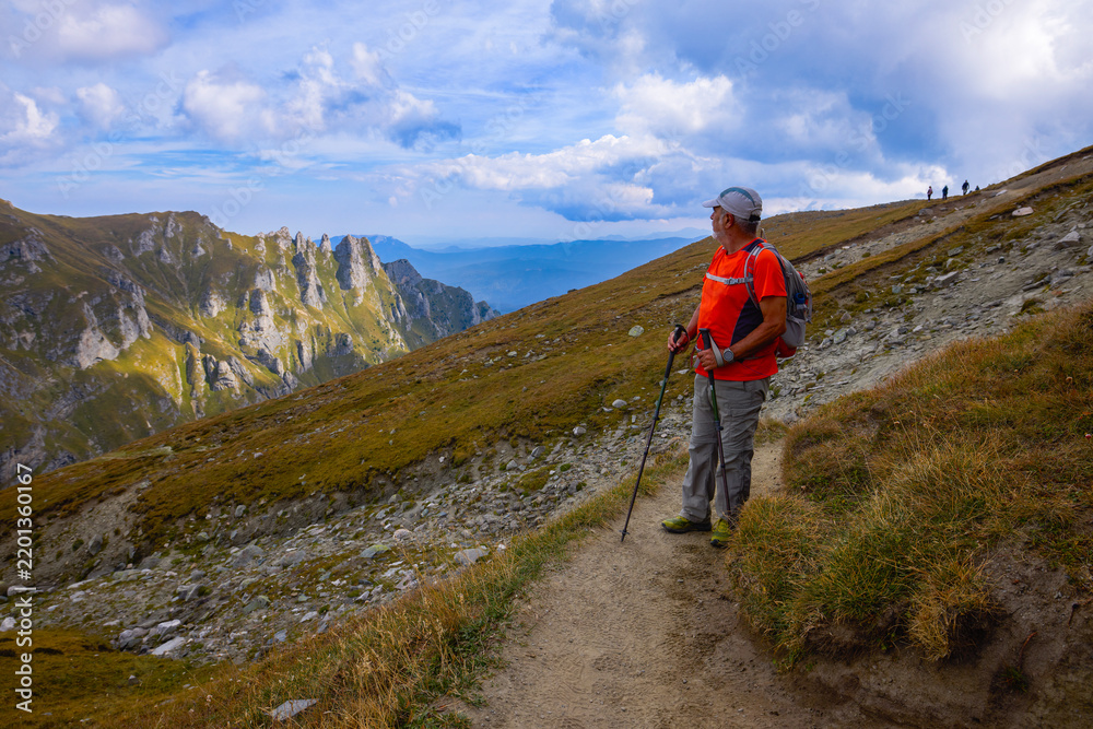Obraz premium a 75-year-old man hiking in the mountains with poles, a backpack, and mountain gear on a beautiful September day
