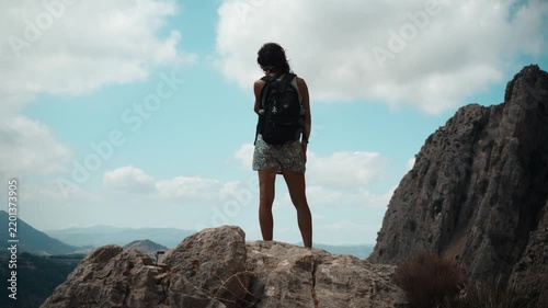 A young woman hiker with a backpack standing on a limestone outcrop gazing at distant mountain ranges under a cloudy sky in El Chorro Andalusia Spain