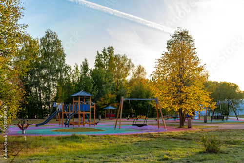 Photography Scenic early autumn view of a modern empty children playground with swings and slides in a public park surrounded by golden trees under a sunny sky, Moscow, Russia